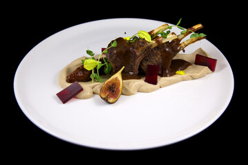 Molecular cuisine. Meat ribs with vegetable puree, decorated with pieces of jelly and figs. On a white plate, on a black background. Beautiful food