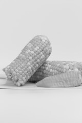 Three ears of fresh, ripe corn on the cob are partially shucked on a white cutting board. A clean...