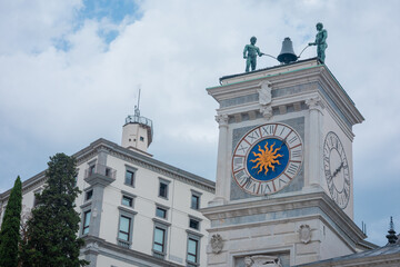Striking view of Udine s Clock Tower in Piazza della Libert , featuring two Moors striking the bell, a sun-decorated clock face, and historic architecture under a cloudy sky.
