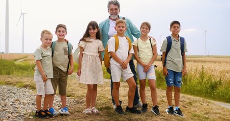 Portrait of a senior teacher with group of school children outdoors in a field with wind turbines, renewable energy education in nature. - Powered by Adobe