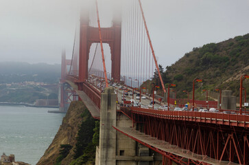 Golden Gate Bridge with heavy traffic and fog, coastline cliffs and old building on San Francisco Bay