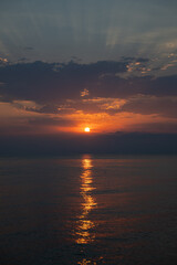 Naklejka premium Dramatic golden sunrise over sea with breaking through dark clouds. Peaceful and serene horizon at dawn as the sun rises and reflects on calm water. Hope and new beginnings