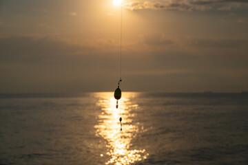 Fishing float hanging with sunrise over the sea. Fishing line silhouette against golden sun with foat dangling. Tranquil morning view