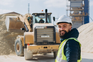 Construction worker smiling at concrete production plant with wheel loader