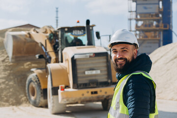 Construction worker smiling at concrete production plant with bulldozer