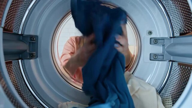 positive young woman putting things in washing machine drum