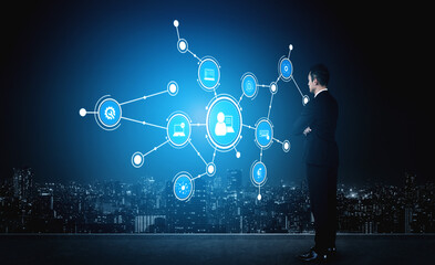 A businessman stands in front of a futuristic digital display, analyzing connections and data visualization against a stunning urban skyline at night. Tessel