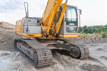 Obraz premium Large yellow excavator, outdoor construction site, dirt ground, sparse vegetation, scattered rocks, soft lighting overcast or late afternoon, realistic style, hydraulic arm, bucket attachment
