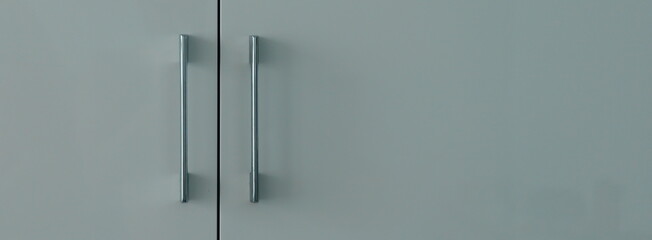 Modern gray cabinet doors with long silver metal handles. Minimalist furniture design detail with clean background and copy space.