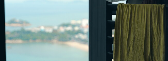 A green towel hanging to dry on a balcony with a beautiful blurry view of the sea and a coastal town in the background. Relaxing vacation concept.