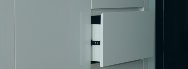 Modern minimalist furniture design with a sleek gray cabinet. Close-up detail of an open handleless drawer showing the black slide mechanism.