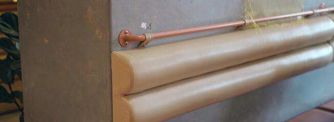 Modern interior design detail of a beige leather upholstered bench with a copper rail against a...