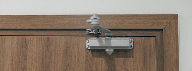 Close-up of an automatic hydraulic door closer mechanism installed on a modern wooden door. Silver door hardware for smooth closing.