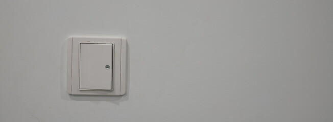 White key-operated light switch on a plain gray wall. Minimalist interior background with ample copy space for text or design.
