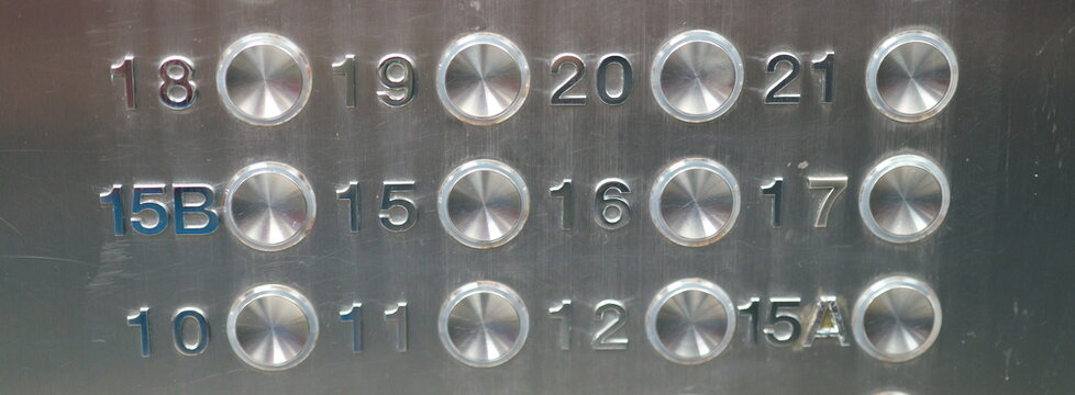 Close up of a scratched brushed metal elevator button panel. Round steel buttons with floor numbers for a high rise building.