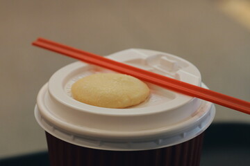 A small sugar cookie resting on the white lid of a disposable coffee cup. A simple sweet snack for a coffee break.
