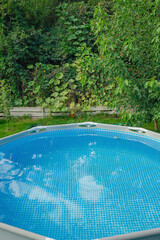 Frame swimming pool with clean water in the garden on a background of nature. Relaxation by the water.