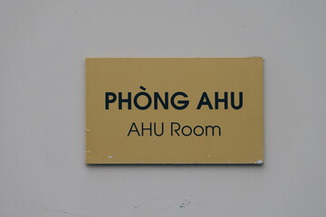 Obraz premium PHÒNG AHU AHU Room sign. Bilingual text in Vietnamese and English on a yellow plaque mounted on a gray wall, indicating an Air Handling Unit room.