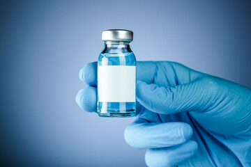 Nurses hand in blue medical gloves holding a medical vaccine vial with blank white copy space for text. Healthcare concept of prevention, treatment, or new pharmaceutical drugs.