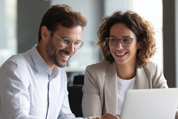 Fototapeta premium two happy professional business people talking in a meeting using laptop computers discussing an online AI project together working in an office at work