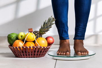 Weight loss journey, African woman on scale with fruit basket. Health, diet, wellness concept.