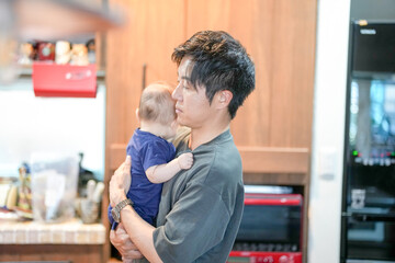 In a Mediterranean-style dining kitchen, a Japanese father in his 30s stands holding a...