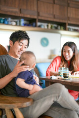 A man is holding a baby while sitting at a table with a woman and a child. Scene is warm and loving, as the family enjoys each other's company