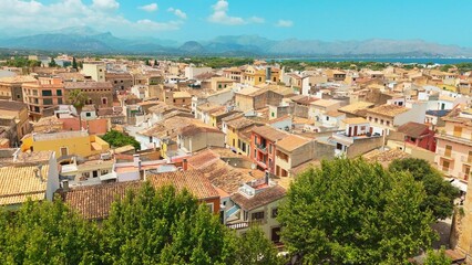 Alcudia, SPAIN Scenic aerial view of vibrant rooftops and lush greenery, showcasing the architectural charm and natural beauty of a coastal town in a sunny Mediterranean landscape