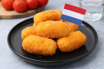 Delicious fried croquettes and flag of Netherlands on gray table, closeup