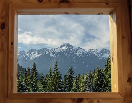 View of towering mountains framed by window as sunset bathes peaks


