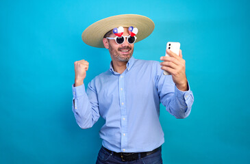 Excited chilean man celebrating online success while holding smartphone and raising fist in front of blue background, national holiday and patriotism celebration 