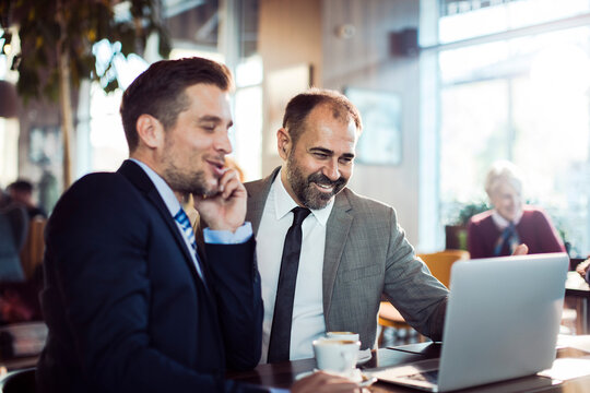 Two businessmen discussing work over laptop in coffee shop