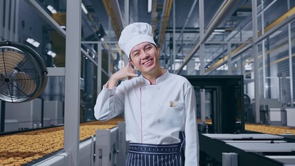 Asian Man Chef Smiling And Making Call Me Gesture To Camera While Standing, Automated Cookie Production Line in Modern Factory