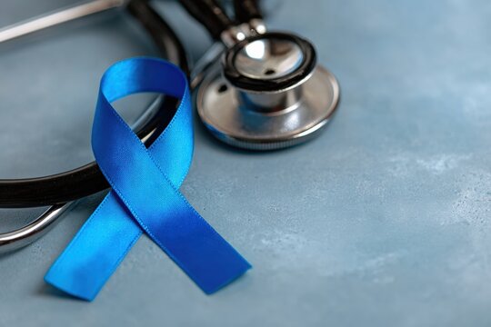 Dark blue awareness ribbon for prostate cancer awareness month and colon cancer awareness month near a stethoscope on a doctor table - Powered by Adobe