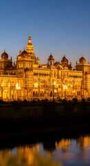 Fototapeta premium The majestic Mysore Palace illuminated with golden lights at dusk, reflecting in the calm water below.