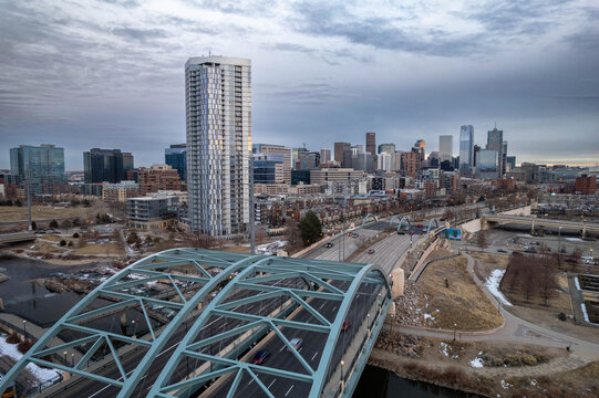 Aerial view of modern city skyline with high-rise buildings, bridge, and river under dramatic cloudy sky in Denver, Colorado, USA. Urban architecture and downtown cityscape at sunrise in winter season