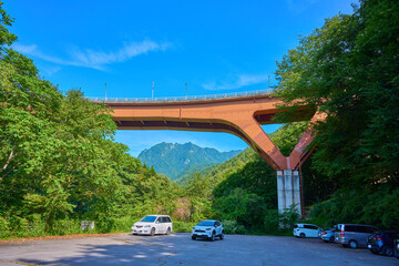 山梨県山梨市の西沢渓谷市営駐車場から笛吹川に架かる西沢大橋越しに鶏冠山を見る