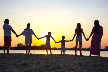 Family gathered at the beach holding hands as the sun sets over the water in summer