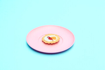 Mini fruit pies on pink plate topped with fruit slices, blue  background