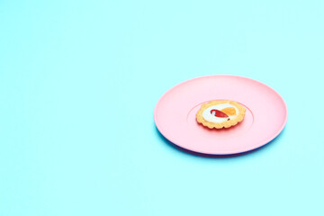 Mini fruit pies on pink plate topped with fruit slices, blue  background