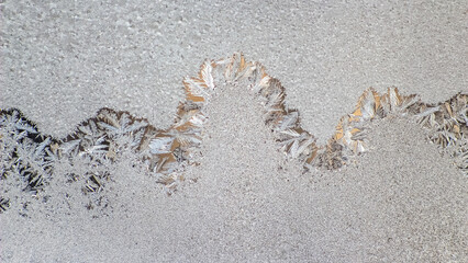 Frost patterns create intricate designs on a window during a cold winter morning