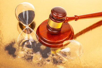 Symbolic representation of time and justice with broken hourglass and gavel on gold surface