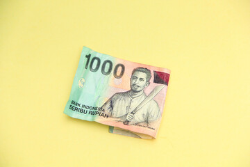 A crisp Indonesian one thousand rupiah banknote placed against a bright yellow background, highlighting its intricate design and cultural symbolism