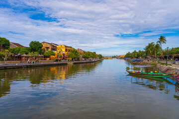 A busy riverbank scene in Hoi An, with numerous colorful tourist boats docked in the foreground and a row of classic yellow buildings in the background.