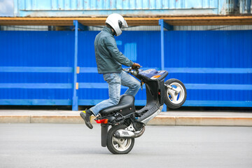 Scooter rider performs wheelie trick on city street in daytime