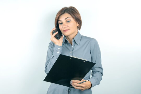Businesswoman making a phone call while reviewing notes in an office setting