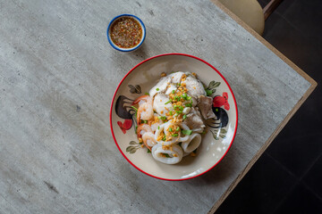 Seafood Dish: An eye-level view showcases a vibrantly colored, appetizing seafood dish, complemented by a small bowl of savory dipping sauce, elegantly presented on a rustic table