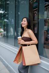 Happy shopper drinking coffee and holding shopping bags is looking away