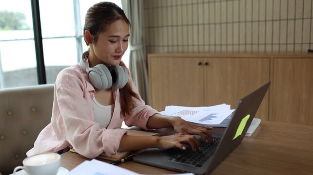 Young female student smiling while studying at desk with laptop and books, engaged in research, e-learning, and university coursework indoors.

