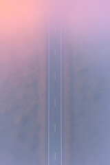 Aerial photo of a straight road cutting through fog at dawn, pastel sky blending with mist for a minimalist and serene atmosphere